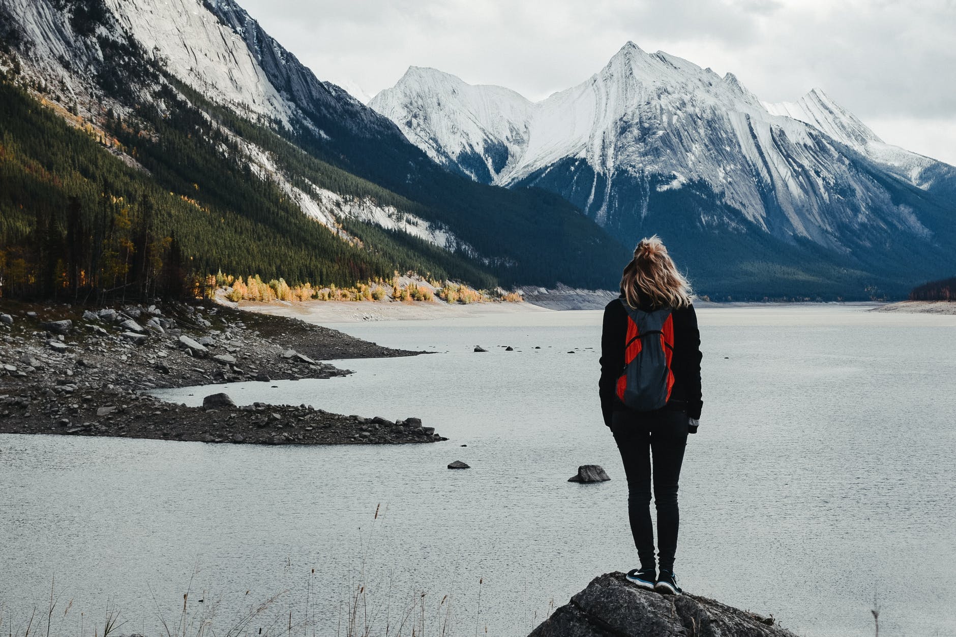 traveler admiring lake surrounded by snowy mountains